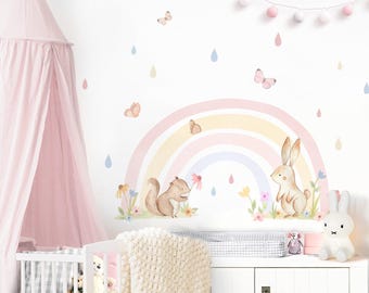 May include: A pastel rainbow wall decal with a squirrel and a rabbit, surrounded by butterflies and raindrops. The decal is on a white wall in a nursery with a pink canopy crib and a white changing table.