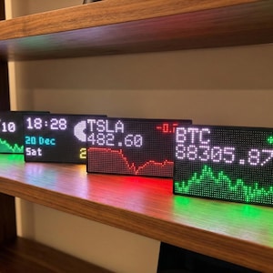 May include: Four LED stock tickers displaying financial data, including AAPL, TSLA, and BTC, with real-time stock prices and percentage changes. The tickers are arranged on a wooden shelf, with green and red lighting.