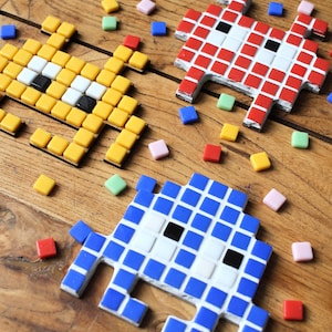 Peut inclure: Trois envahisseurs spatiaux en pixel art faits de carreaux colorés. Les envahisseurs spatiaux sont jaunes, rouges et bleus. Les carreaux sont disposés en grille pour créer l'art pixel.