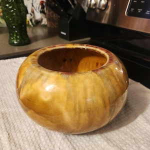 May include: A round, glazed ceramic bowl with a wide opening. The bowl features a blend of warm colors, including shades of brown, yellow, and a hint of red around the rim. The glossy finish enhances the colors and texture of the pottery.