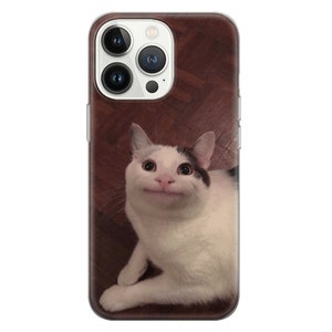 May include: A white and black cat with large, wide eyes and a big smile. The cat is lying on a brown wooden floor. The cat is looking directly at the camera.