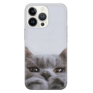 May include: A gray cat with yellow eyes peeks out from the bottom of a clear phone case. The case is designed for an iPhone with a camera bump on the back.