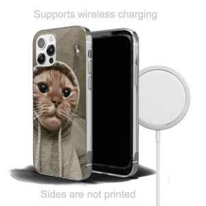 May include: A clear phone case with a cute cat wearing a grey hoodie printed on the back. The case is compatible with wireless charging. The image also shows a wireless charging pad.