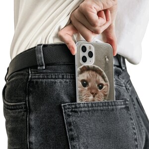May include: A clear phone case with a picture of a cat peeking out of the top. The case is in a back pocket of a pair of dark gray jeans.