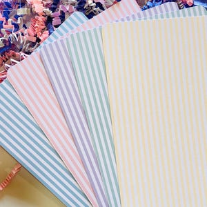 May include: Five striped cards in different colours, including light blue, pink, purple, green, and yellow. The cards are stacked on top of each other, with the yellow card on top.