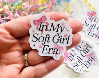 May include: A white sticker with pink bows and flowers. The sticker says "In My: Soft Girl Era".