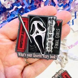 Può includere: Una spilla in smalto nero, bianco e rosso con una maschera di Scream e tre dorsi di libri. I libri sono intitolati "Babysitter Blood", "Clown in the Cornfield" e "Final Girls". La spilla include anche il testo "What's your favorite scary book?"
