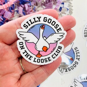 May include: A white sticker featuring a cartoon goose illustration. The sticker has the text "SILLY GOOSE ON THE LOOSE CLUB" in a circular design. The background is a gradient of pink and blue.
