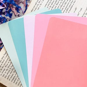 Op de afbeelding: Een stapel van vijf pastelkleurige kaarten in tinten roze, blauw en groen. De kaarten zijn rechthoekig met afgeronde hoeken en liggen op een open boek. De kaarten zijn blanco en klaar voor gebruik.