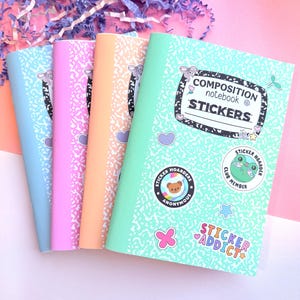 May include: Four composition notebooks with speckled covers in light blue, pink, peach, and mint green. The front notebook features a label reading COMPOSITION notebook STICKERS and various circular and shaped stickers including a bear and a frog.