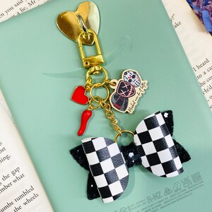 Pode incluir: Um porta-chaves dourado com um berloque em forma de coração, um coração vermelho e um berloque de pimenta vermelha. Também apresenta um laço xadrez em preto e branco e um pequeno berloque com uma figura mascarada e o texto "Mashed men do it better."