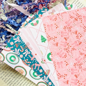 Op de afbeelding: Een stapel kerstkaarten met verschillende patronen. Ontwerpen omvatten zuurstokken, strikken, kerstbomen en peperkoekhuisjes in roze, blauwgroen en wit. De kaarten zijn gerangschikt op een vintage pagina.
