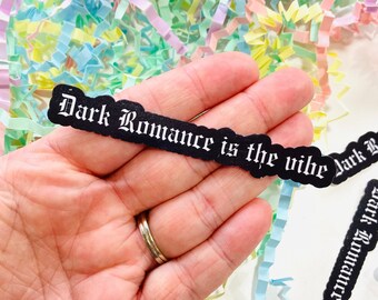 May include: A black sticker with white gothic lettering that reads "Dark Romance is the vibe".