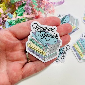 May include: A sticker with a stack of books and the text "Romance Reader" in a colorful, whimsical font. The books have titles like "Fake Relationship", "Enemies To Lovers", "Best Friend's Brother", and "Slow Burn".