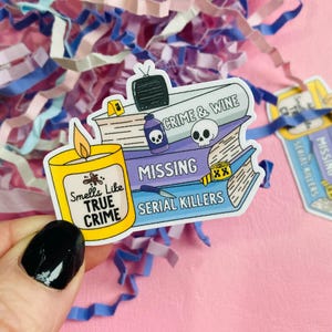 May include: A sticker set featuring a candle and a stack of books with the words "Crime & Wine", "Missing", and "Serial Killers". The candle reads "Smells Like True Crime". The stickers are on a pink background with colorful paper shreds.
