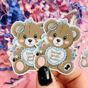 May include: Two brown teddy bear stickers with blue bows, floral accents, and heart-shaped details. Each bear holds a heart with text that reads "Dear Gentle Reader" and "Dear Gent Read". A small bee is also featured.