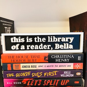 Może przedstawiać: Stos książek z białą ramką z napisem "this is the library of a reader, Bella". Książki mają różne tytuły i kolory, w tym "The House That Horror Built" i "Let's Split Up".