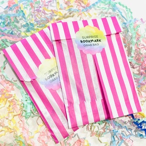 Può includere: Due sacchetti di carta a righe rosa e bianche con un adesivo bianco che dice "Surprise Bookmark Grab Bag" su ogni sacchetto.