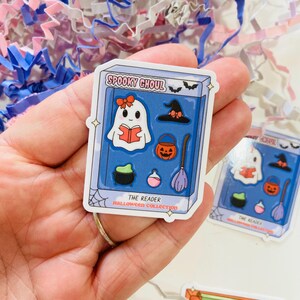 May include: A sticker featuring a cartoon ghost reading a book, with a witch hat, jack-o'-lantern, cauldron, potion bottle, and broom. The sticker is labeled "Spooky Ghoul" and "The Reader Halloween Collection."