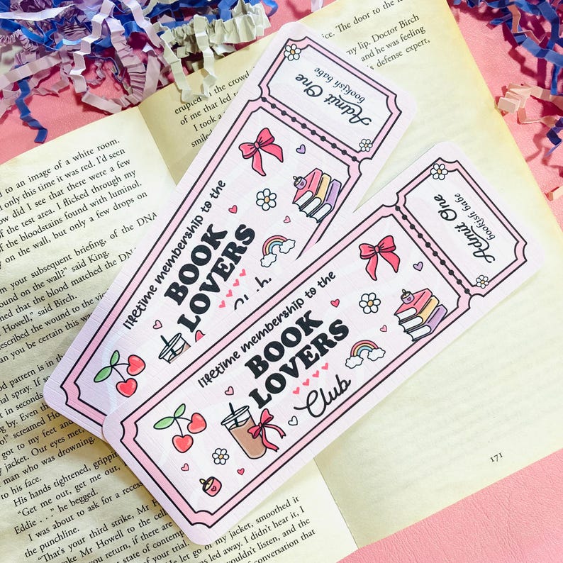 Może przedstawiać: Dwie r&oacute;żowe zakładki w kształcie biletu z zaokrąglonymi rogami. Zakładki mają napis "lifetime membership to the BOOK LOVERS Club" oraz ilustracje wiśni, tęczy i książek.