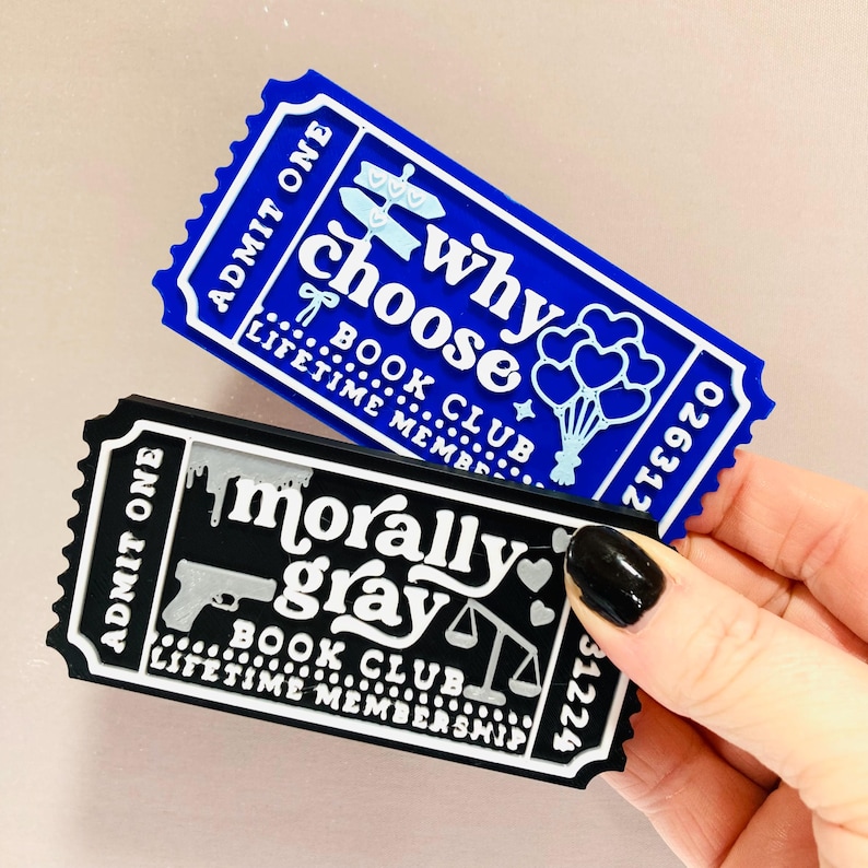 Op de afbeelding: Twee magneetjes in de vorm van een ticket. E&eacute;n is blauw met de tekst "why choose BOOK CLUB LIFETIME MEMBERSHIP". De andere is zwart met "morally gray BOOK CLUB LIFETIME MEMBERSHIP". Beide hebben de tekst "ADMIT ONE".
