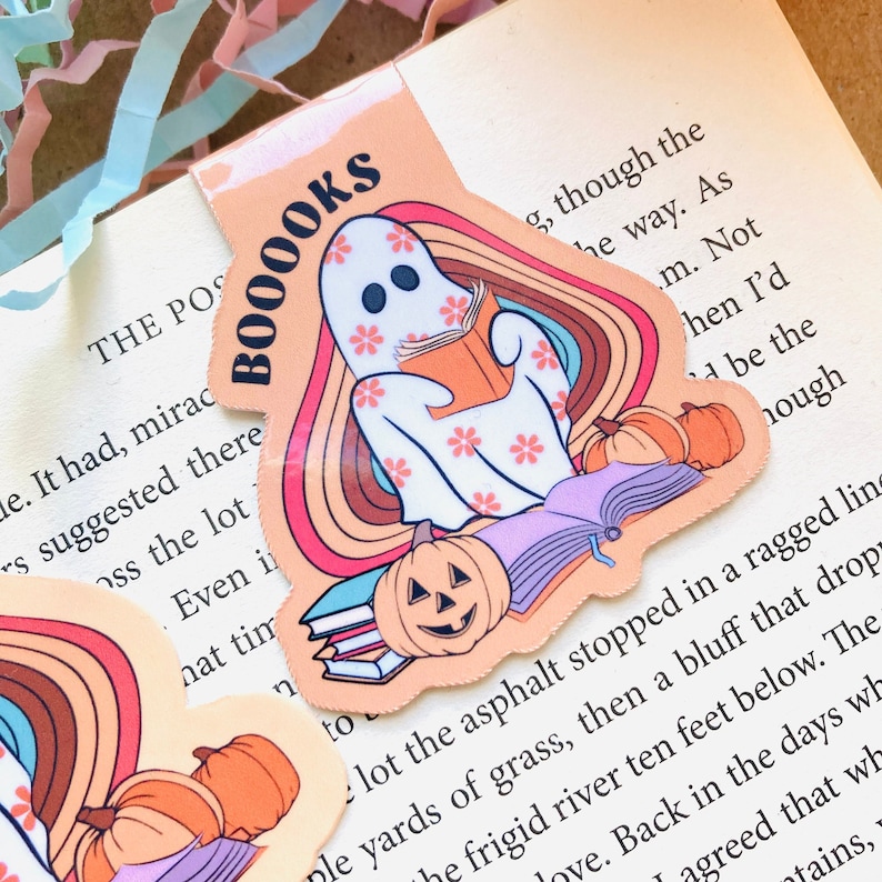 Peut inclure: Un marque-page color&eacute; avec un fant&ocirc;me lisant un livre, une pile de livres et des citrouilles. Le marque-page porte le texte "BOOOOKS" dans une police r&eacute;tro.