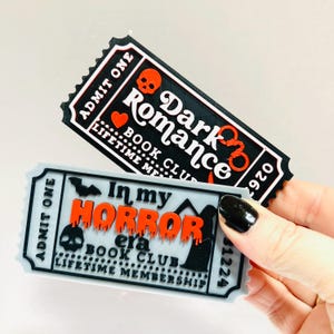 Op de afbeelding: Twee stickers in de vorm van een ticket met gotische thema's. E&eacute;n leest "Dark Romance Book Club" met een schedel en een hart. De andere zegt "In my Horror Era Book Club" met een vleermuis, schedel en grafsteen. Beide hebben de tekst "Admit One".