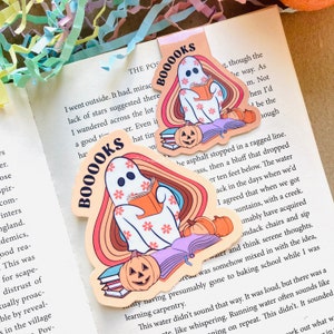 Peut inclure: Un autocollant color&eacute; repr&eacute;sentant un fant&ocirc;me lisant un livre avec une pile de livres et une citrouille d'Halloween. L'autocollant porte les mots "Booooks" dans une police r&eacute;tro.