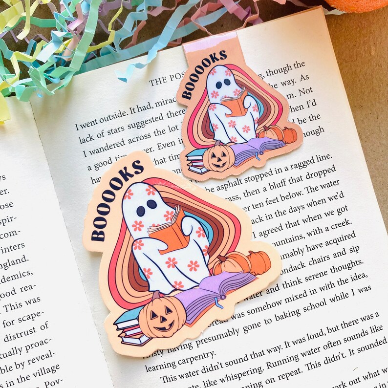 Peut inclure: Un autocollant color&eacute; repr&eacute;sentant un fant&ocirc;me lisant un livre avec une pile de livres et une citrouille d'Halloween. L'autocollant porte les mots "Booooks" dans une police r&eacute;tro.