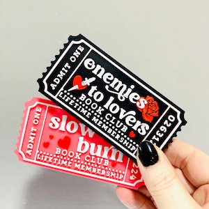 Op de afbeelding: Twee rechthoekige stickers met een ticketontwerp. E&eacute;n is zwart met de tekst "enemies to lovers BOOK CLUB LIFETIME MEMBERSHIP". De andere is rood met de tekst "slow burn BOOK CLUB LIFETIME MEMBERSHIP".