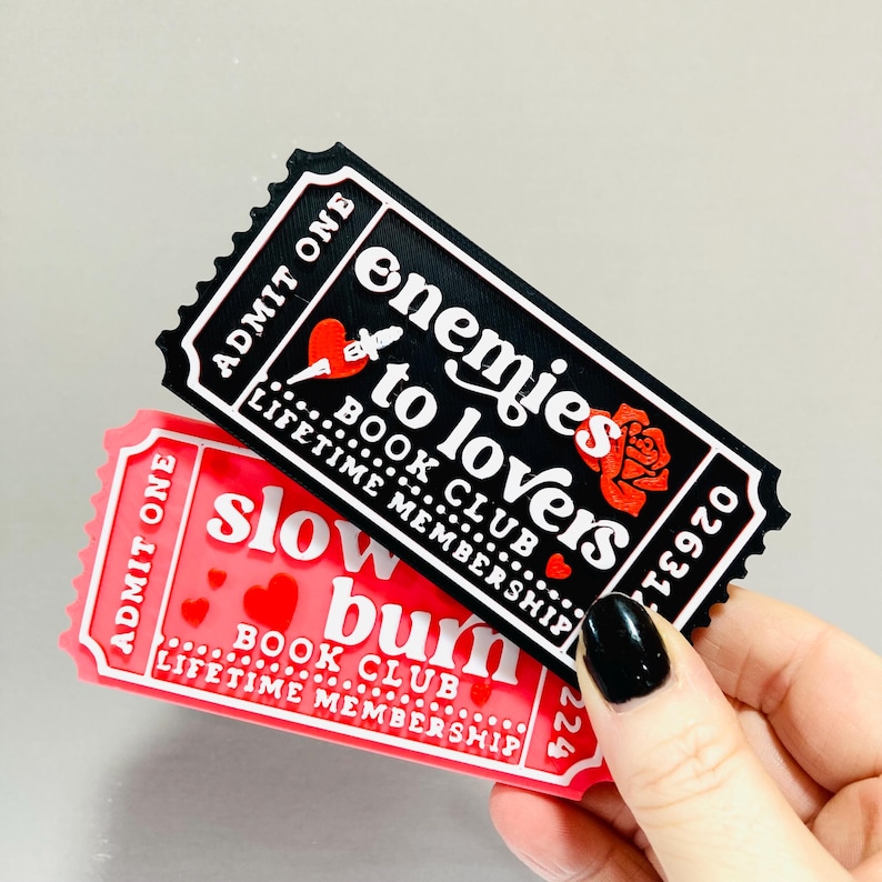 Op de afbeelding: Twee rechthoekige stickers met een ticketontwerp. E&eacute;n is zwart met de tekst "enemies to lovers BOOK CLUB LIFETIME MEMBERSHIP". De andere is rood met de tekst "slow burn BOOK CLUB LIFETIME MEMBERSHIP".