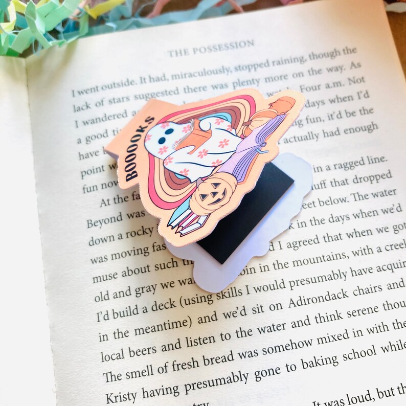 Peut inclure: Un marque-page color&eacute; avec un fant&ocirc;me tenant un livre, une citrouille et une pile de livres. Le marque-page porte le texte "BOOOOKS".