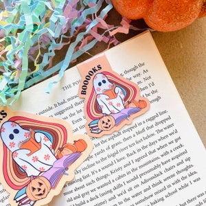 Peut inclure: Deux marque-pages fant&ocirc;mes color&eacute;s avec un fond arc-en-ciel, une pile de livres et une citrouille d'Halloween. Le marque-page dit "Booooks" en lettres noires.