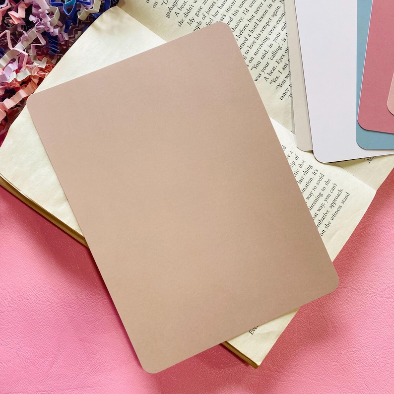 May include: A rectangular, light brown card with rounded corners, resting on an open book with aged pages. The card is the focal point, with a soft, matte finish. Other cards are visible in the background.