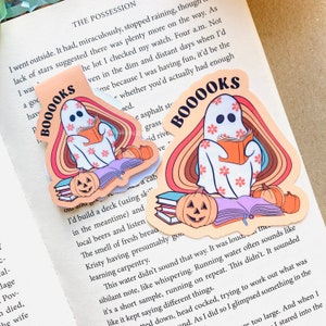 Peut inclure: Un autocollant repr&eacute;sentant un fant&ocirc;me lisant un livre avec le texte "Booooks" en couleurs arc-en-ciel et une pile de livres surmont&eacute;s de citrouilles.