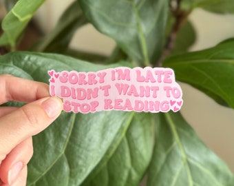 May include: Pink sticker with the text "Sorry I'm late I didn't want to stop reading" with pink hearts on either side.