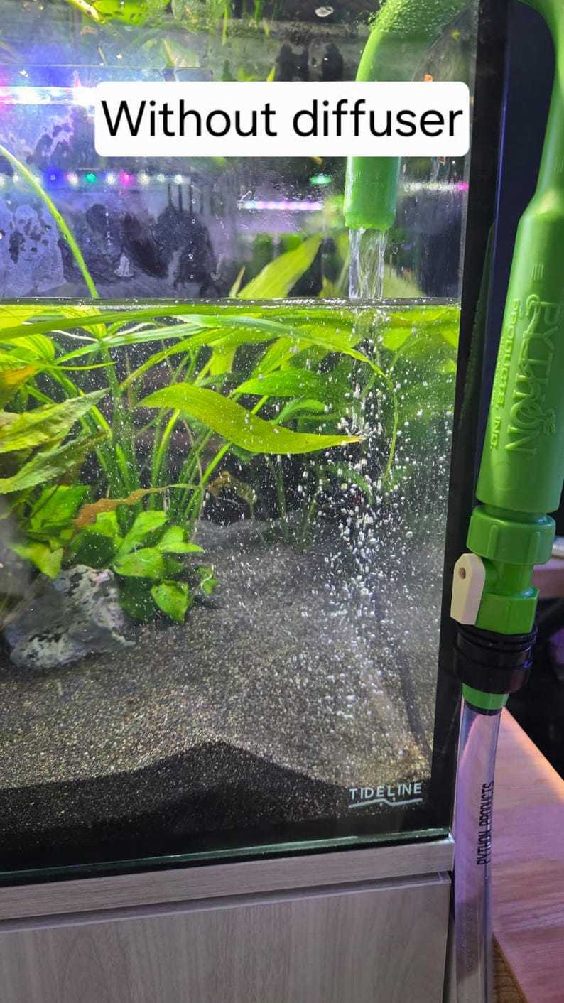 May include: An aquarium with aquatic plants and a dark substrate. Water flows from a green tube, creating bubbles. The text "Without diffuser" is displayed above the tank. A green and white siphon is visible on the right side of the image.