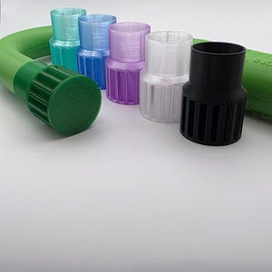 May include: A collection of colorful, cylindrical plastic adapters in various colors, including teal, blue, purple, clear, and black. A green hose is visible on the left and right sides of the image. The adapters have a ribbed design.