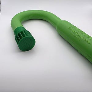 May include: A green, curved cane-shaped product with a textured, dark green cap. The product is made of a solid, smooth material. The text "PRODUCTS, INC. MADE IN THE USA" is printed on the side.