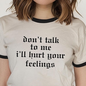 Könnte beinhalten: Weißes T-Shirt mit schwarzem Text, der "don't talk to me i'll hurt your feelings" in gotischer Schrift lautet. Das Shirt hat einen schwarzen Ringel.