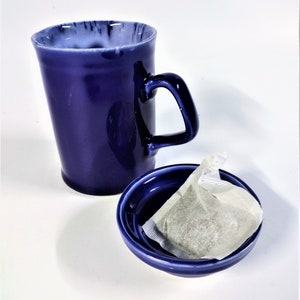 May include: A blue ceramic teacup and saucer with a white tea bag inside the saucer.