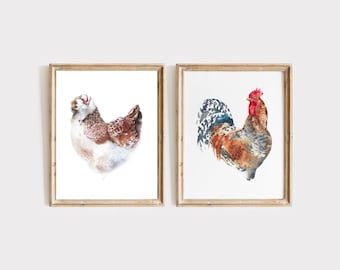 May include: Two framed wall art prints featuring watercolor illustrations of poultry. The left print shows a brown and white hen, while the right print depicts a rooster with brown, grey, and red plumage. Both are in light wood frames.