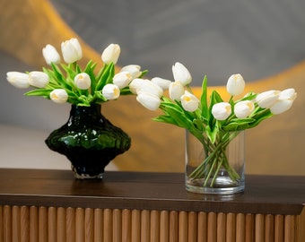 Peut inclure: Deux bouquets de tulipes blanches, l'un dans un vase vert foncé et l'autre dans un vase en verre transparent, sur une table en bois avec un motif nervuré.