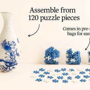 May include: A white vase with blue floral designs stands next to three bags of blue and white puzzle pieces. The text reads "Assemble from 120 puzzle pieces" and "Comes in pre-sorted bags for easy build".