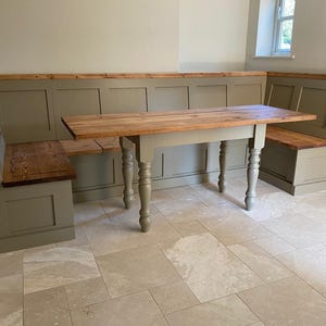 May include: An L-shaped corner bench and a rectangular dining table. The bench features sage green paneled bases with natural wood seats and top rails. The table has a matching natural wood top and four sage green turned wooden legs.