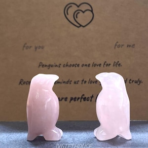 May include: Two pink quartz penguin figurines. The penguins are standing in front of a brown card with the text "Always, you and me" and "Penguins choose one love for life." The card also has a heart design.
