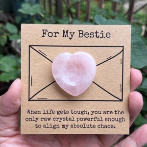 May include: A pink heart-shaped crystal rests on a brown card with the text "For My Bestie." The card also features the text "When life gets tough, you are the only raw crystal powerful enough to align my absolute chaos."