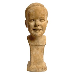 Puede incluir: Un busto de escultura de terracota de un niño pequeño con una expresión sonriente. El busto está montado sobre una base rectangular.
