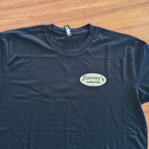 May include: Black t-shirt with a light green oval logo that says "Jimmy's Smoked Meats" on it.