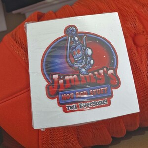 May include: White sticker with a red, blue, and black logo for Jimmy's Hot Rod Stuff. The logo features a cartoon robot holding a wrench and the text "Tell Everyone!"